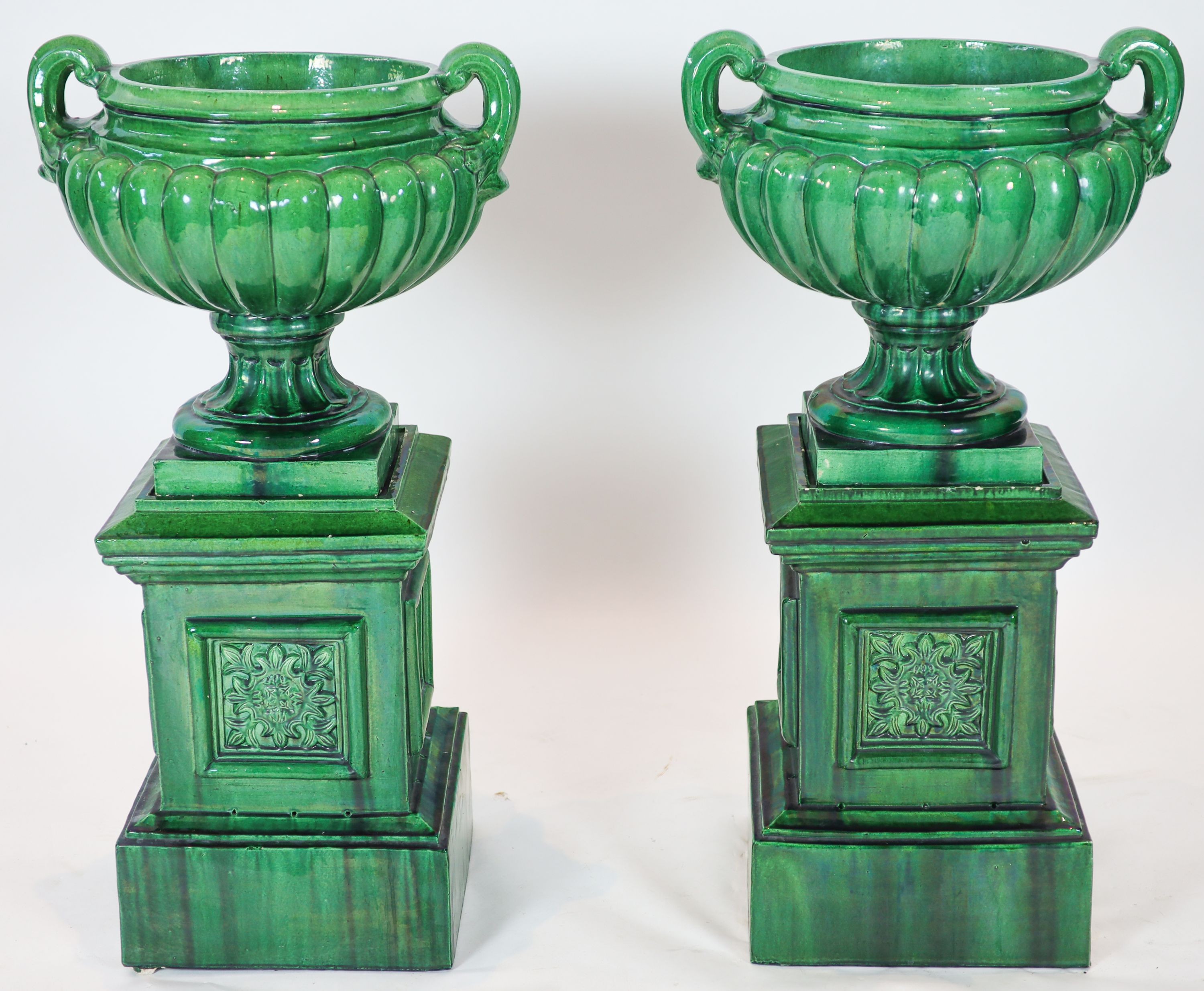 A pair of large dark green glazed terracotta fluted urns, raised on square plinths, diameter 50cm, height 101cm